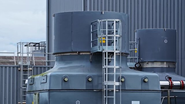 Aerial view of industrial cooling tower labeled TAR 2 at a power plant facility with metal structures and ladders in Europe.