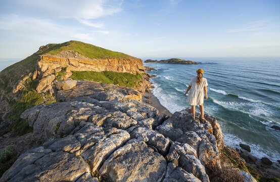 Young pretty woman wearing dress off coast and sea at Robberg Nature Reserve, Plettenberg Bay, South Africa