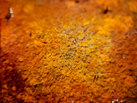 Extreme close-up macro photograph showing the heavily oxidized, flaking, and bright orange crusty texture of severely corroded metal.