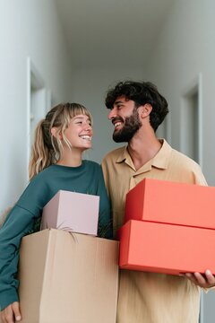 Young couple holding colorful boxes in narrow hallway smiling for moving announcement poster background and relocation banner design
