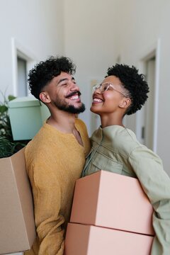 Joyful young couple carrying moving boxes and laughing in a bright hallway for relocation banner and social media background