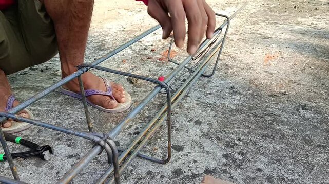 Close-up footage of a worker tying reinforcing steel bars for reinforced concrete construction