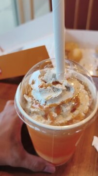 Hand holds creamy caramel topped iced drink with straw at wooden table