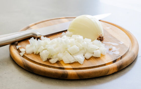 Chopped White Onion and Chef Knife on Round Wooden Cutting Board Close Up