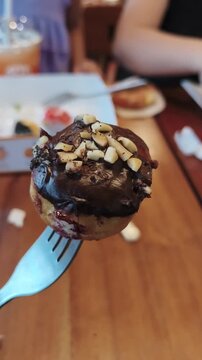 Chocolate donut topped with nuts on fork being lifted from plate