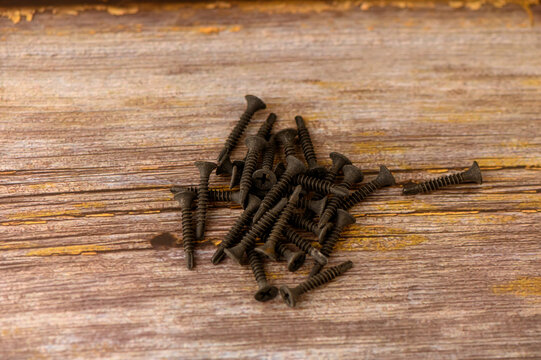 Various black screws lay haphazardly on an aged, weathered wooden table, showcasing an intricate dance of shadows and texture. The scene captures the essence of craftsmanship and the tools of creation