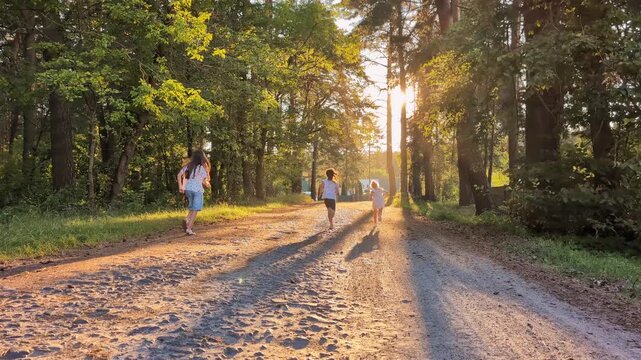 Three children walk along a dirt path in a forest during sunset. They hold hands and spend time together in nature, surrounded by trees and sunlight