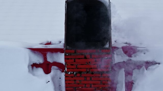 Aerial view of a red brick chimney stack protruding from a snow-covered rooftop during winter, Europe.