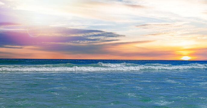 A serene ocean view at sunset featuring gentle waves crashing along the shoreline under a colorful sky.
