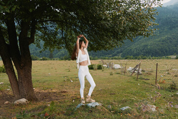 Woman in white dances under a tree in a sunlit meadow, enjoying carefree lifestyle moments in a...