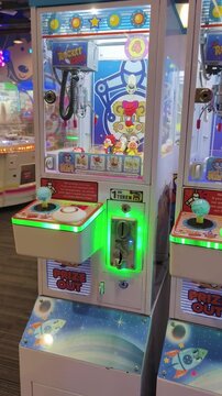 Child plays claw machine game in arcade pulling lever to win prize.