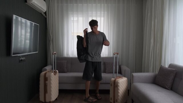 Business traveler arriving at hotel apartment. Man entering temporary accommodation with luggage and looking around after journey