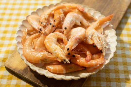Boiled unshelled tiger shrimps on plate on yellow white tablecloth. Seafood.
