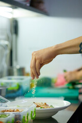 Fototapeta premium Chef seasoning fresh salad during plate assembly in commercial kitchen. Concept of restaurant plating, fresh meal preparation, professional food service.