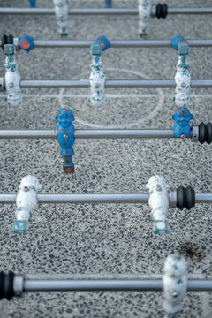 Close-up of worn blue and white foosball player figures on metal rods above a speckled tabletop with shallow depth of field