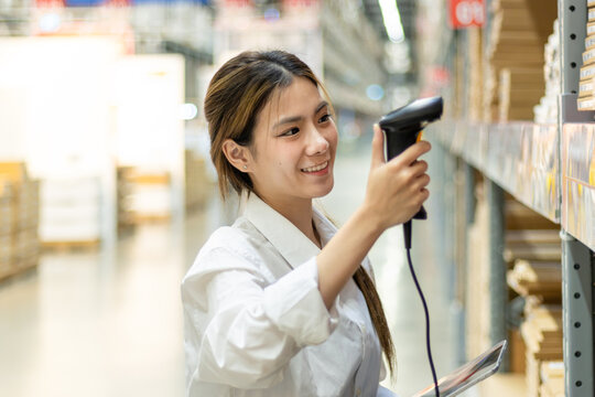Asian woman worker with tablet using laser barcode reader to scan stock inventory in warehouse. Young beautiful female logistic staff scans the barcode of products on shelves in wholesale warehouse.