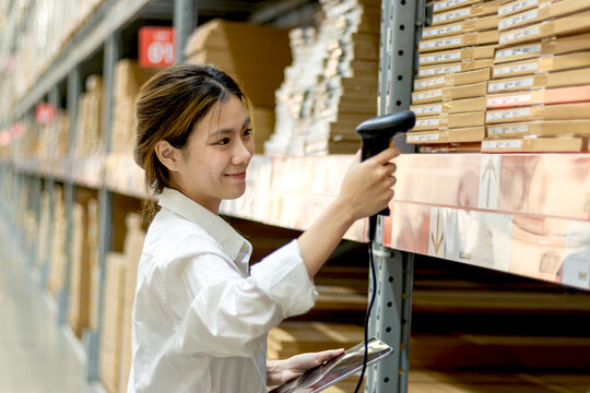 Asian woman worker with tablet using laser barcode reader to scan stock inventory in warehouse. Young beautiful female logistic staff scans the barcode of products on shelves in wholesale warehouse.