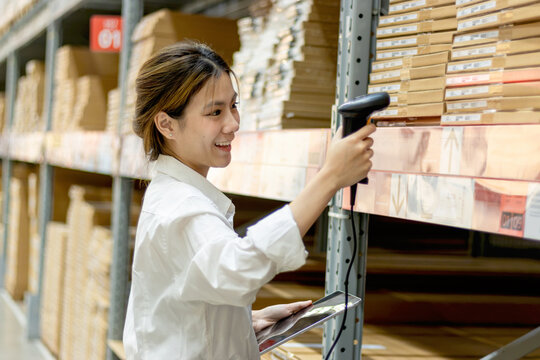 Asian woman worker with tablet using laser barcode reader to scan stock inventory in warehouse. Young beautiful female logistic staff scans the barcode of products on shelves in wholesale warehouse.