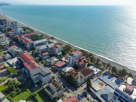Kobuleti city featuring an urban sprawl along the black sea coast, showcasing residential buildings, hotels, and the beach with mountains in the distance under a clear sky