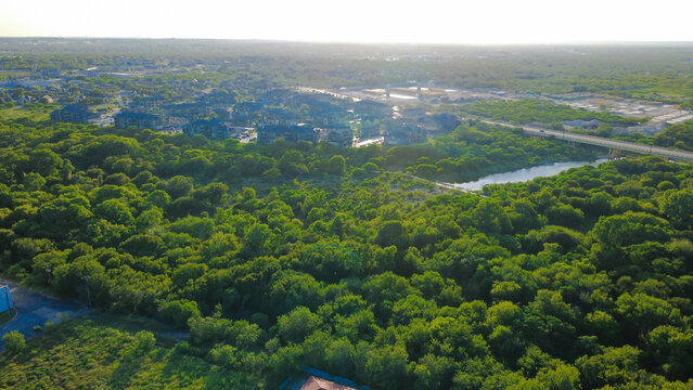 Thick green treetops along Leon Creek Greenway in Greater San Antonio sweep toward distant concrete roadway bridge in San Antonio, Texas. Residential communities border forested corridor horizon