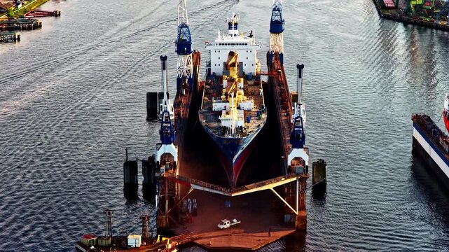 Aerial view of a large cargo ship undergoing maintenance in a floating dry dock at a shipyard in Europe.