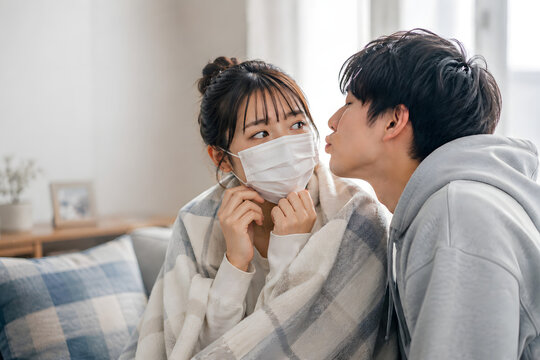 Young Man Trying to Kiss a Woman Wearing a Face Mask at Home
