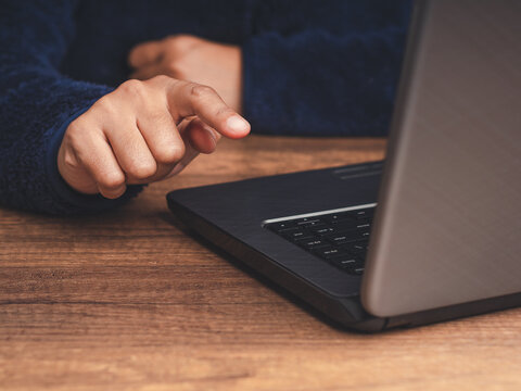 Person Pointing Toward Laptop on Wooden Desk
