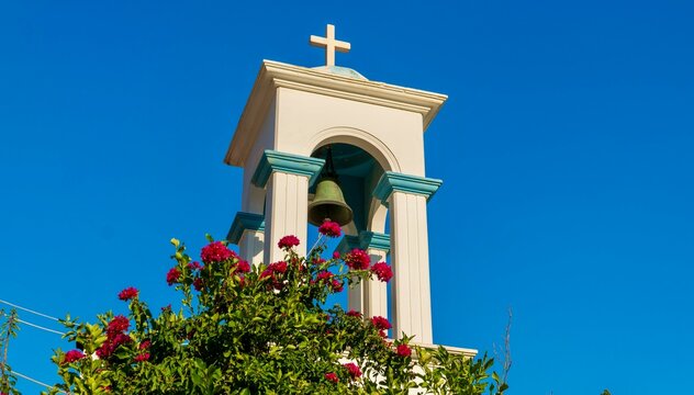 Pythagoreio, Greece - August 1, 2026: View of the bell tower at Panagia Spiliani Holy Monastery on Samos Island, showing white Greek Orthodox architecture, bell, cross and stone details