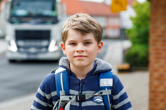 Little elementary Schoolboy with backpack smiling on a residential street while walking to school during a typical morning routine. happy child on the way to school