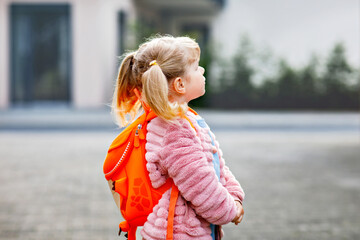 Fototapeta premium Little girl with backpack smiling outdoors on her way to kindergarten, enjoying an independent childhood moment before the school day. Happy preschool child.