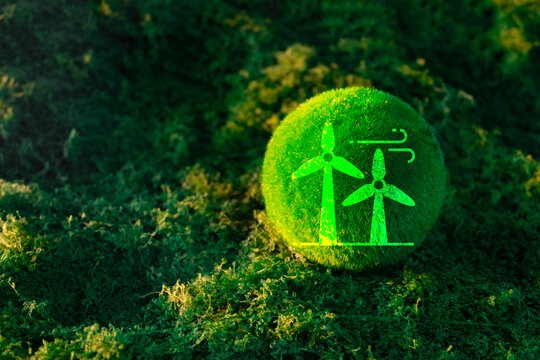 Renewable wind energy and sustainable power concept. A green moss ball displaying a digital wind turbine graphic, resting on a natural mossy background in warm sunlight.