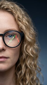 A woman's face with wavy hair and stock chart reflecting on her glasses.
