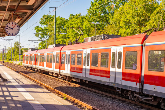 Red and white regional train stopped railway station platform with large clock, sunny summer day, public transport concept, German Deutsche Bahn S-Bahn, boarding travelers in cars, GERMANY hessen