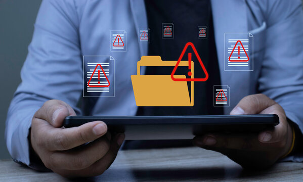 Businessman holding tablet with warning icons on document folders. Corporate professional detecting document fraud and security threat to prevent data leak and risk.