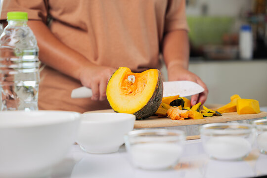 Housewife hands make dessert, cooking sweet food using ingredients like pumpkin and sugar in kitchen, preparing healthy meal with knife on cutting board, water bottle and bowls on table