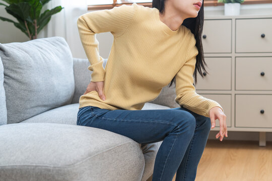 Close-up woman massaging her lower back has back pain because of sitting posture during work in office.
