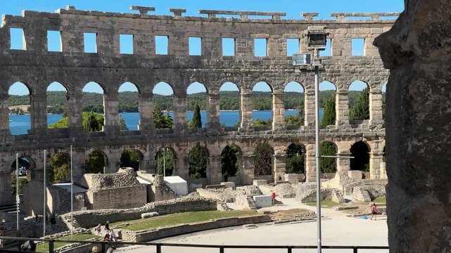 Ancient Roman amphitheater Pula, Croatia features arched openings and a weathered stone facade under a clear blue sky, highlighting its architectural beauty and historical context