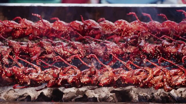 Close up of grilled quails turning on rotating spit at asian street food market.