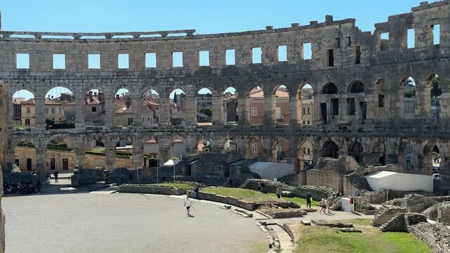 Ancient Roman amphitheater Pula, Croatia features arched openings and a weathered stone facade under a clear blue sky, highlighting its architectural beauty and historical context
