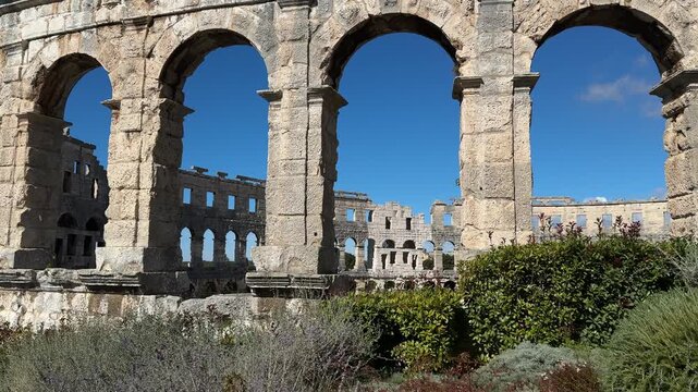 Ancient Roman amphitheater Pula, Croatia features arched openings and a weathered stone facade under a clear blue sky, highlighting its architectural beauty and historical context