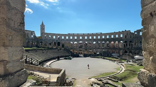 Ancient Roman amphitheater Pula, Croatia features arched openings and a weathered stone facade under a clear blue sky, highlighting its architectural beauty and historical context