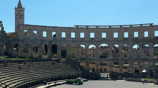 Ancient Roman amphitheater Pula, Croatia features arched openings and a weathered stone facade under a clear blue sky, highlighting its architectural beauty and historical context