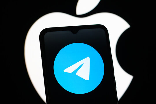 In this photo illustration, the Telegram logo is seen displayed on a smartphone screen and the Apple logo in the background.