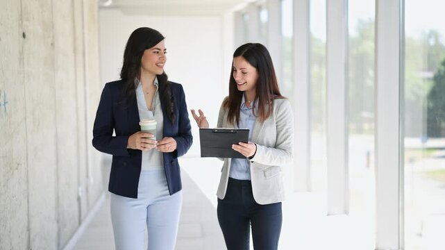 Two female colleagues discussing business in office hallway