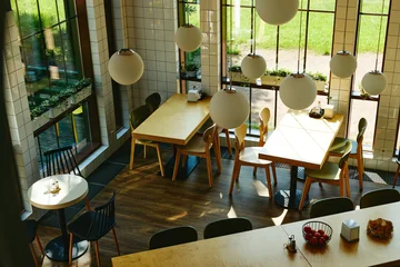 Fototapete Gastronomie Empty modern cafe interior with wooden tables and chairs illuminated by sunlight, representing hospitality business and dining concepts, suitable for restaurant marketing, high angle view  © Seventyfour