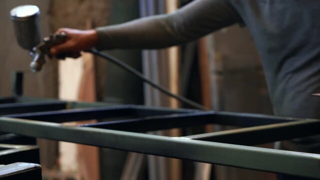Spray Painting Iron Stairs in Workshop
 An industrial worker cleans and spray paints a steel iron stair structure inside a welding workshop, demonstrating metal fabrication, protective coating