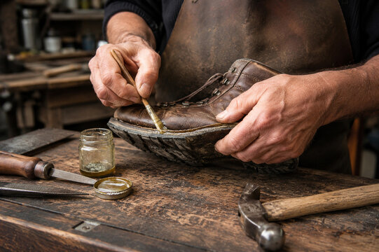 Professional cobbler repairing worn leather work boot with adhesive during traditional shoe restoration in workshop