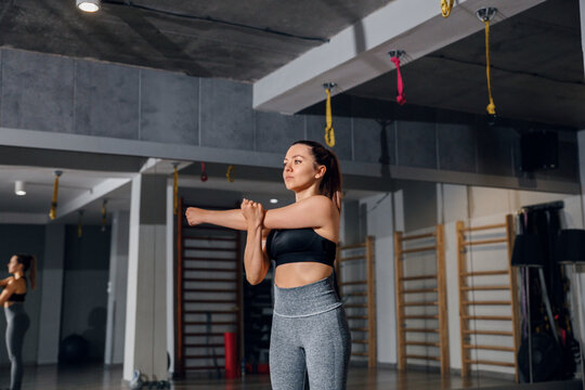 Woman stretching arm across chest with steady posture. Portrait of female model preparing for workout, gym fitness concept.