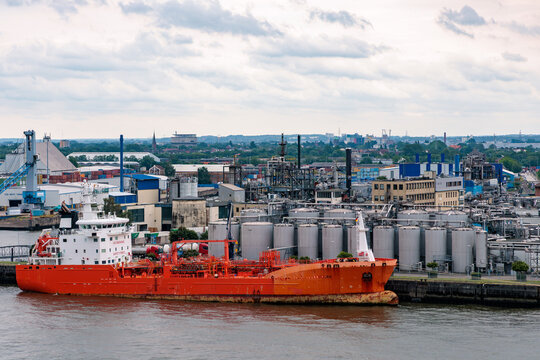 Red chemical tanker ship docked at industrial port terminal with oil refinery storage tanks in Port of Hamburg, global energy logistics concept