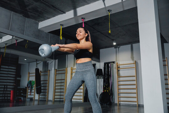 Female athlete performing kettlebell swing with confident posture. Fitness woman improving strength and endurance in gym, functional training concept.